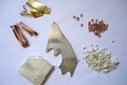 Sheets and granules of gold, copper, brass and silver on a white surface